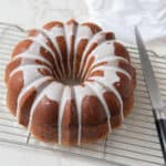 Golden brown bundt cake with white icing drizzle on a wire cooling rack, served as a delicious dessert or centerpiece for celebrations. Perfect for special occasions or tea time.