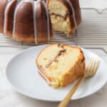 Fresh vanilla chiffon cake with chocolate chip filling, topped with white icing drizzle, on a white plate with a gold fork in front of a cooling rack. Perfect for dessert or tea time.