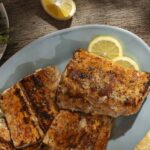 Succulent grilled salmon fillets garnished with lemon slices on a light blue plate, featuring a rustic wooden table setting with fresh asparagus and lemon wedges for healthy, delicious seafood meals.