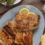 Juicy grilled salmon fillets garnished with lemon slices on a blue plate, served on a rustic wooden table with fresh asparagus and a yellow patterned napkin for a healthy seafood dinner.