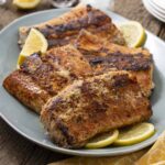 Juicy grilled salmon fillets with crispy skin, seasoned with herbs and spices, served with lemon wedges on a light blue plate. Perfect for a healthy dinner or seafood meal.