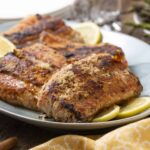 Juicy, seasoned baked salmon fillets with lemon slices on a white serving platter, garnished for a delicious, healthy seafood meal.