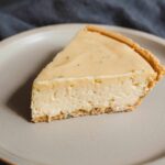 Creamy homemade cheesecake with a graham cracker crust on a beige plate.
