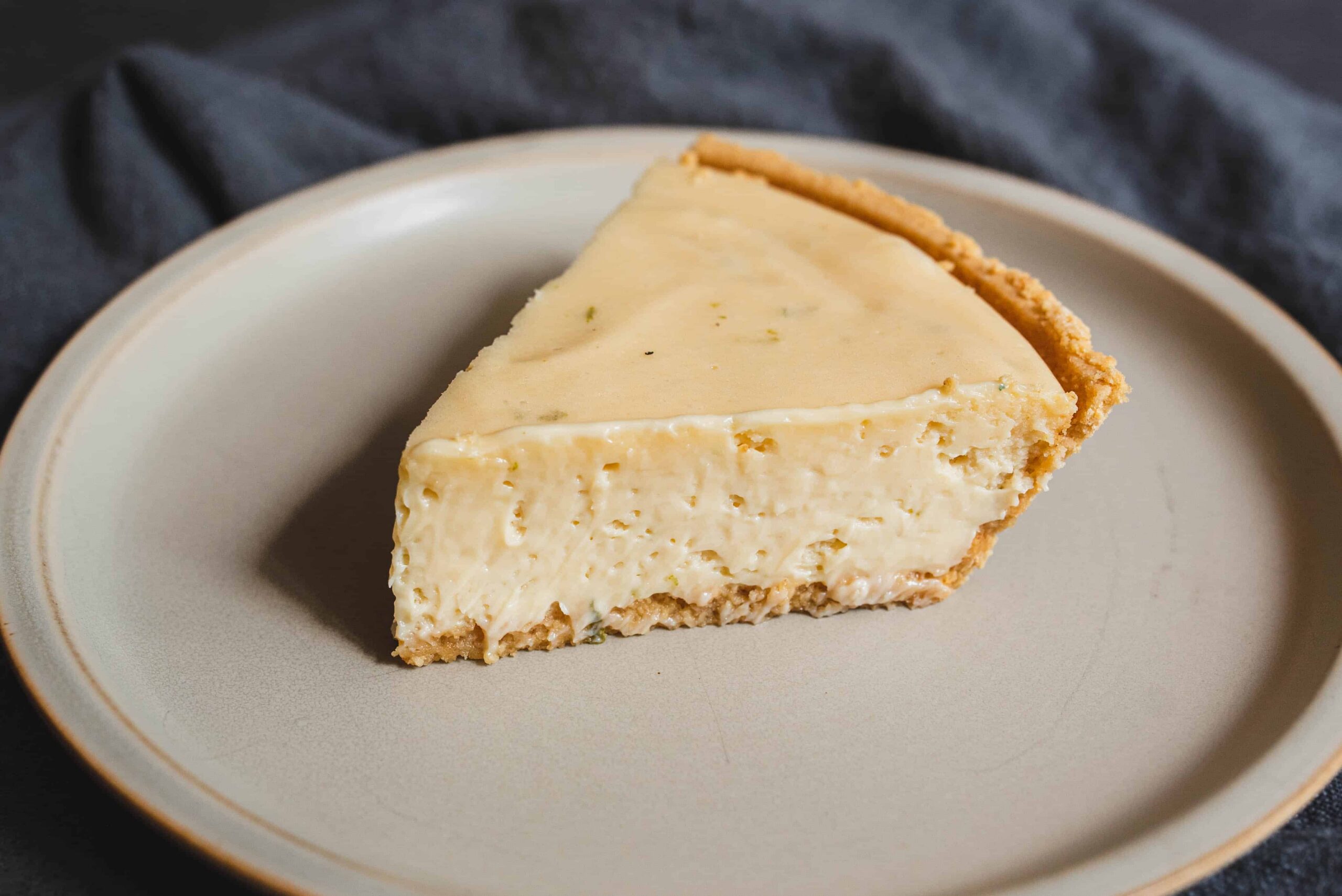 Creamy homemade cheesecake with a graham cracker crust on a beige plate.
