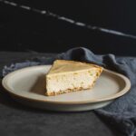 Rich creamy cheesecake slice on a beige plate with dark backgrounds and fabric, delicious easy dessert recipe, classic baked cheesecake for dessert lovers, decadent cheesecake dessert image.