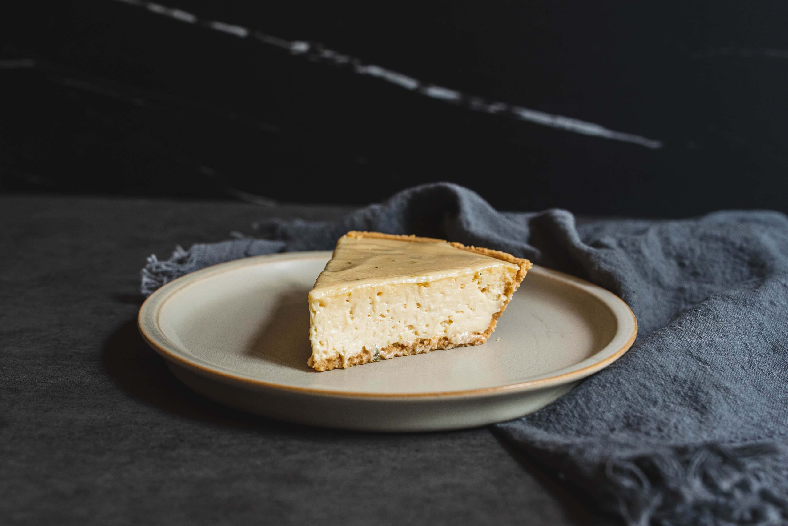 Rich creamy cheesecake slice on a beige plate with dark backgrounds and fabric, delicious easy dessert recipe, classic baked cheesecake for dessert lovers, decadent cheesecake dessert image.