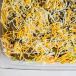 Shredded cheese topping over vegetable casserole in a glass baking dish.