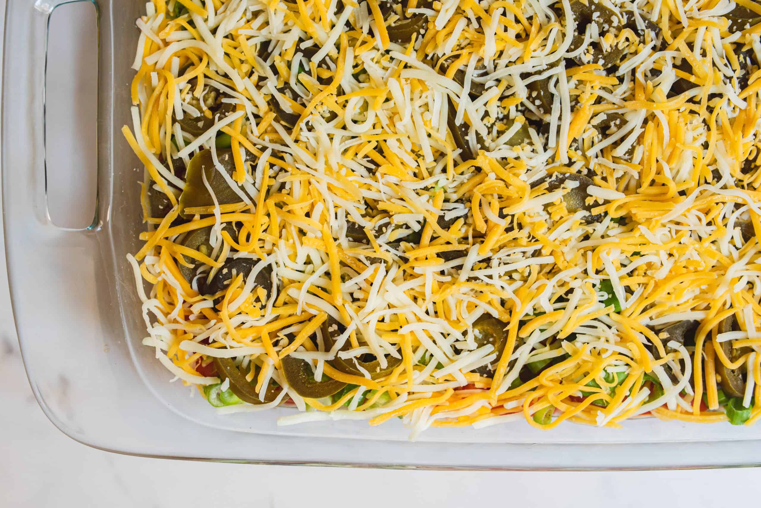 Shredded cheese topping over vegetable casserole in a glass baking dish.