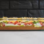 Fresh layered taco dip with beans, cheese, tomatoes, green onions, and sour cream in a glass dish for appetizer or party platter.