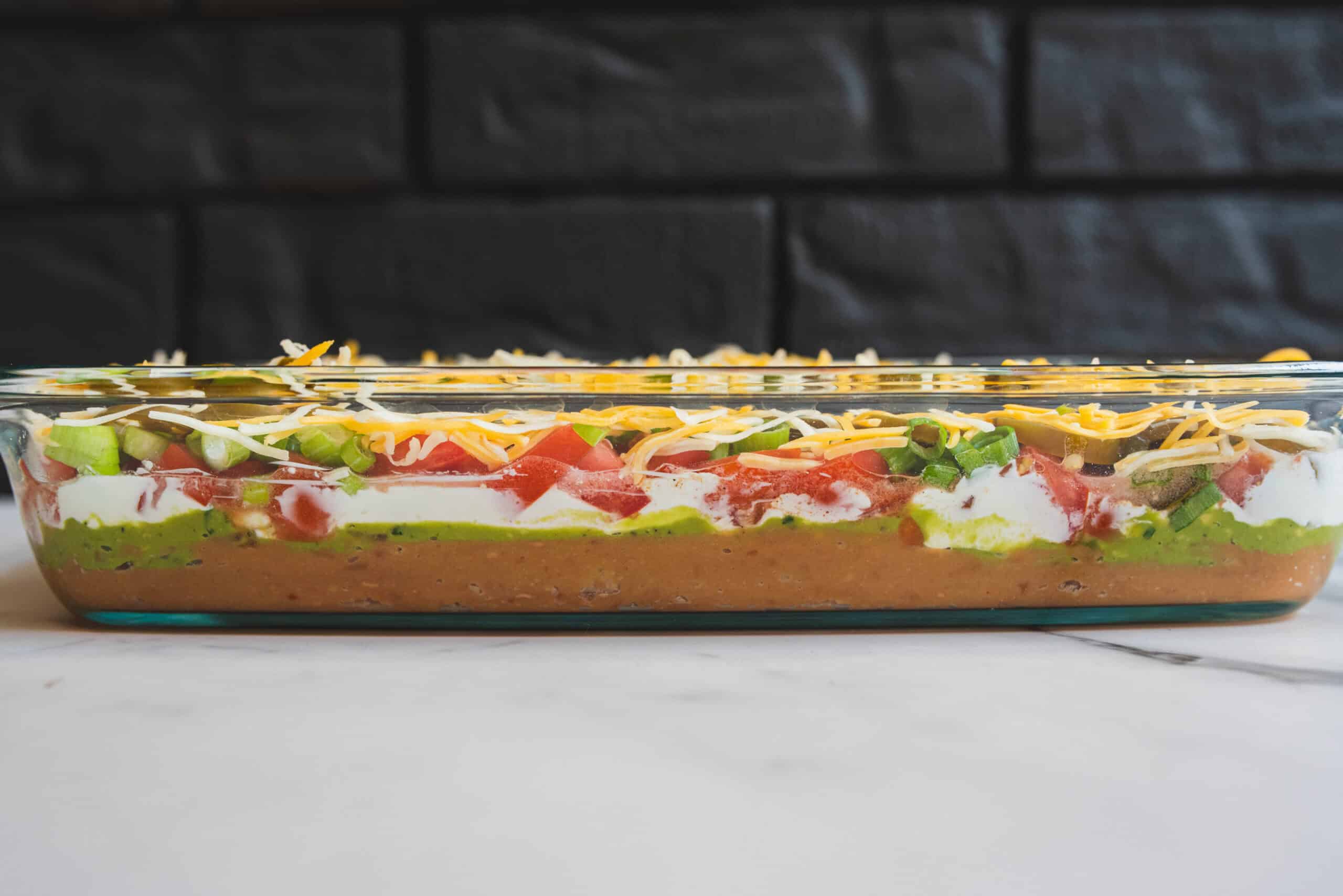 Fresh layered taco dip with beans, cheese, tomatoes, green onions, and sour cream in a glass dish for appetizer or party platter.
