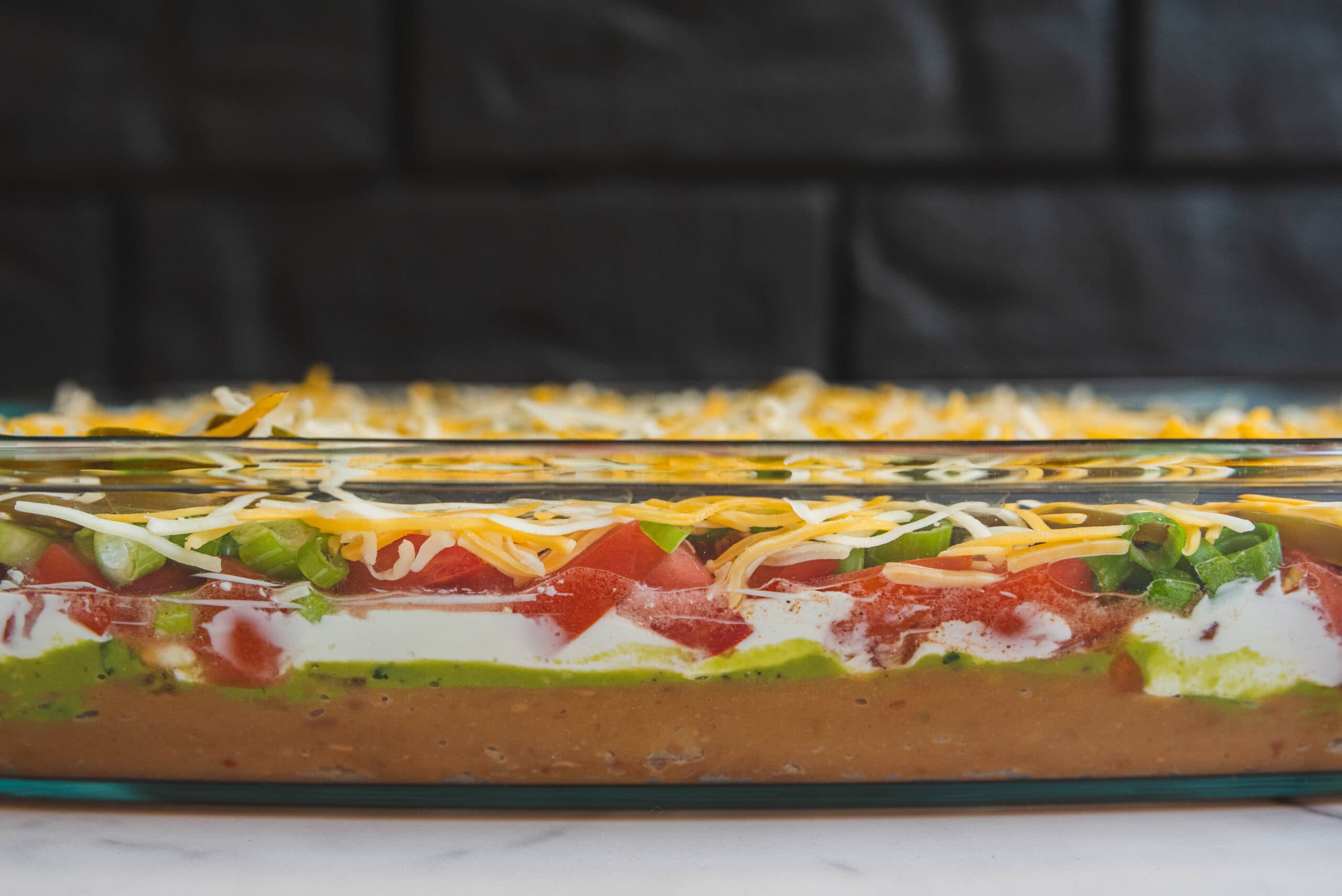 Layers of fresh vegetables, cheese, and creamy sauce in a glass baking dish for delicious casserole or layered dip. Perfect for easy, colorful party recipes and homemade comfort food.