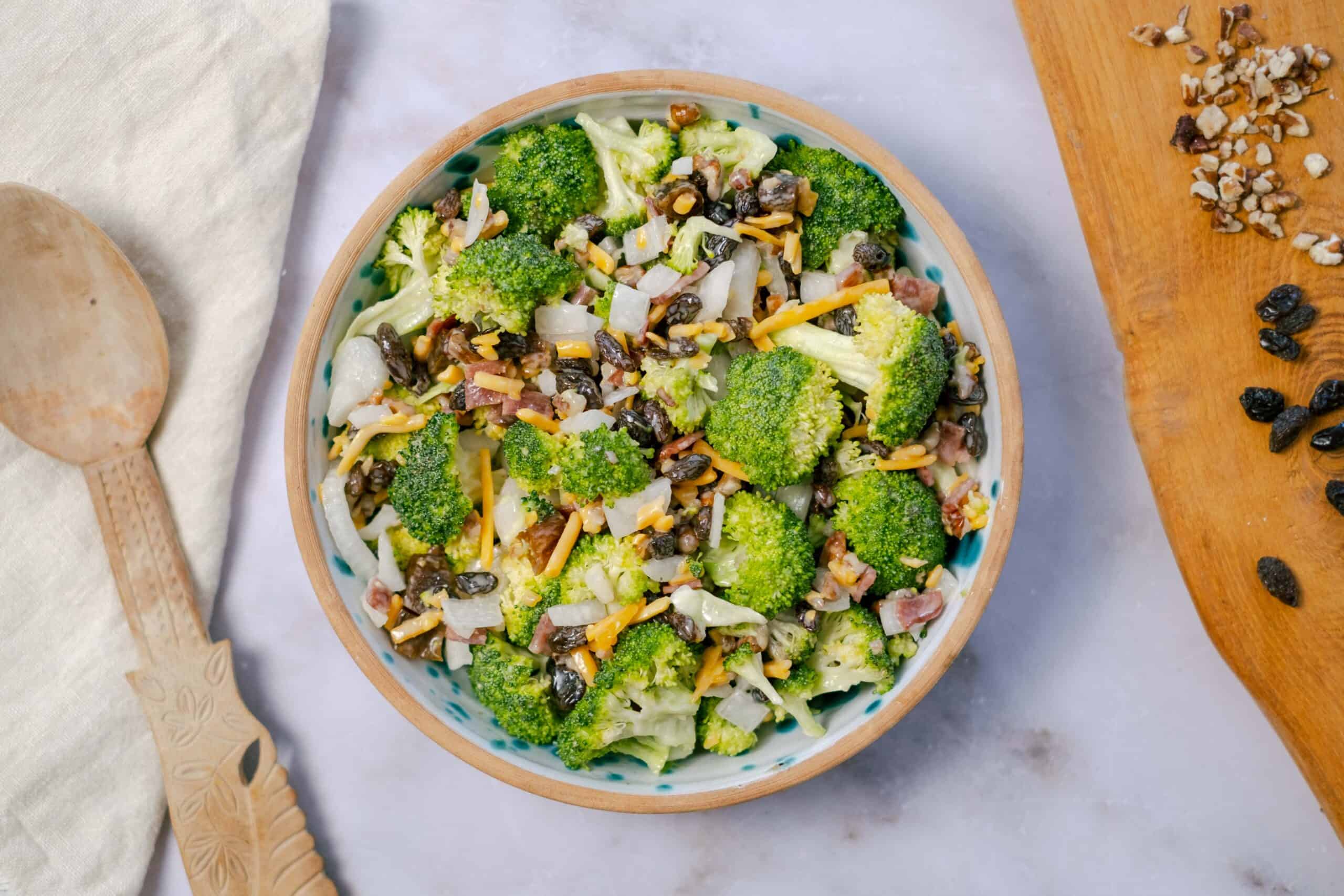 Fresh broccoli and vegetable salad with shredded cheese, black beans, and diced onions in a decorative ceramic bowl.