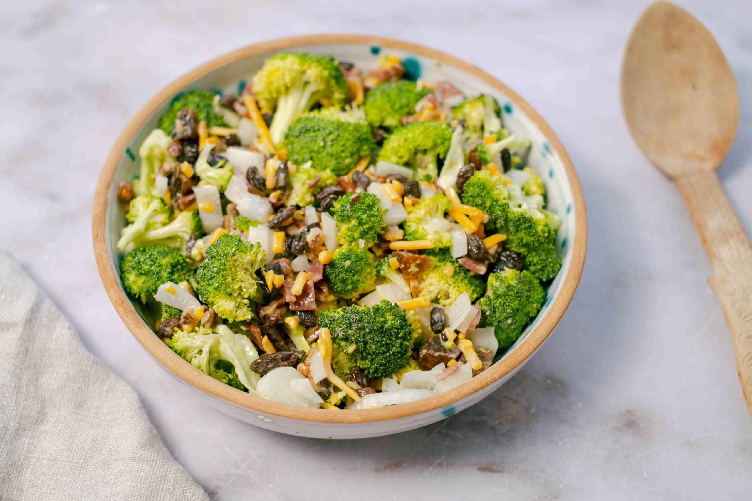 Fresh broccoli salad with cheese, onions, bacon bits, black beans, and shredded cheese served in a decorative bowl for a healthy, tasty meal.