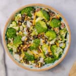 Fresh broccoli salad with shredded cheese, bacon bits, sunflower seeds, and chopped onions in a wooden bowl. Healthy and tasty vegetable side dish for any meal.