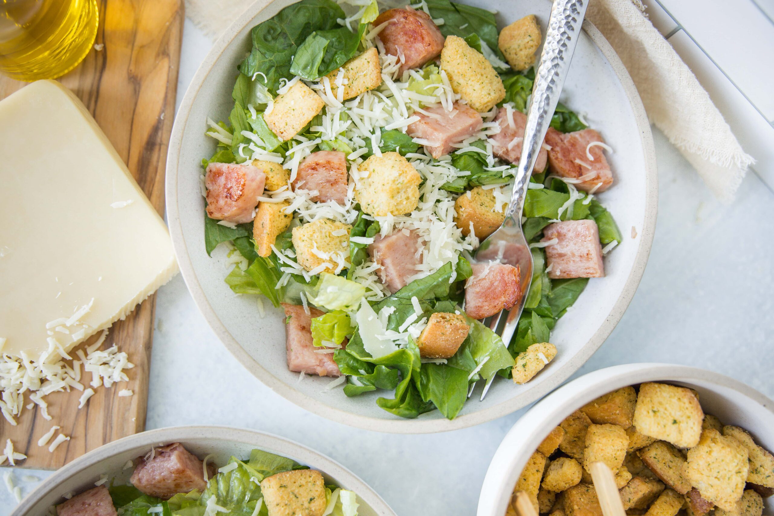 Fresh Caesar salad with crisp romaine lettuce, grilled chicken, shredded Parmesan cheese, and crunchy croutons on a light-colored bowl, served with side dishes on a rustic table.