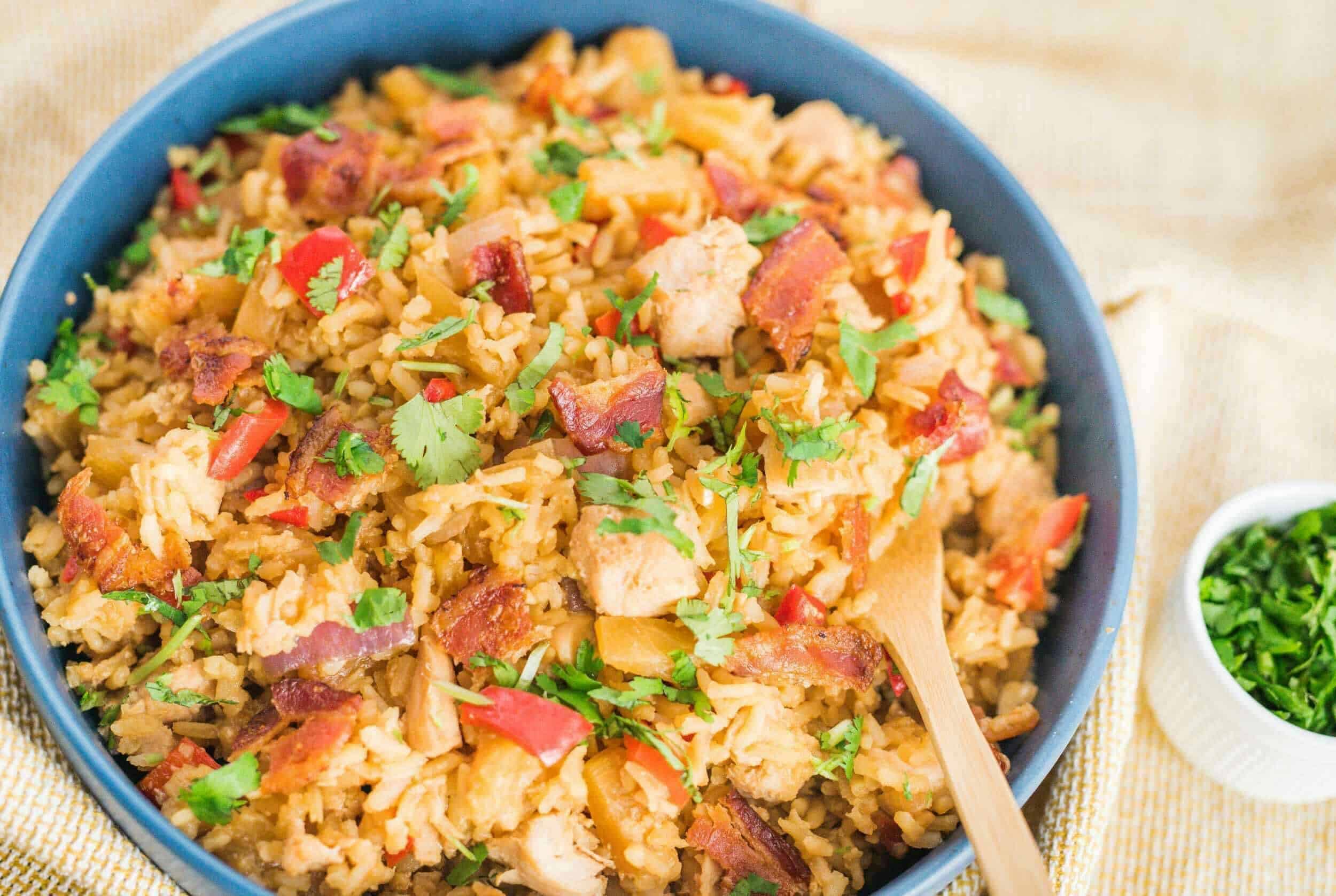 Savory fried rice with chicken, bacon, and vegetables in a blue bowl, garnished with fresh cilantro and served with chopped green herbs. Perfect as a quick and flavorful meal or side dish.