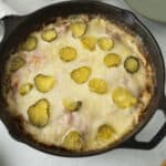 Creamy baked cheese casserole topped with sliced pickles, served in a cast iron skillet, perfect for comfort food and snack recipes.