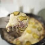 Sliced casserole dish with ham, cheese, and pickles on a spatula, ready to serve; baked casserole with melted cheese and toppings.