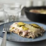 Baked chicken casserole with pickles and melted cheese served on a blue plate, with a fork, in a cozy home kitchen setting.