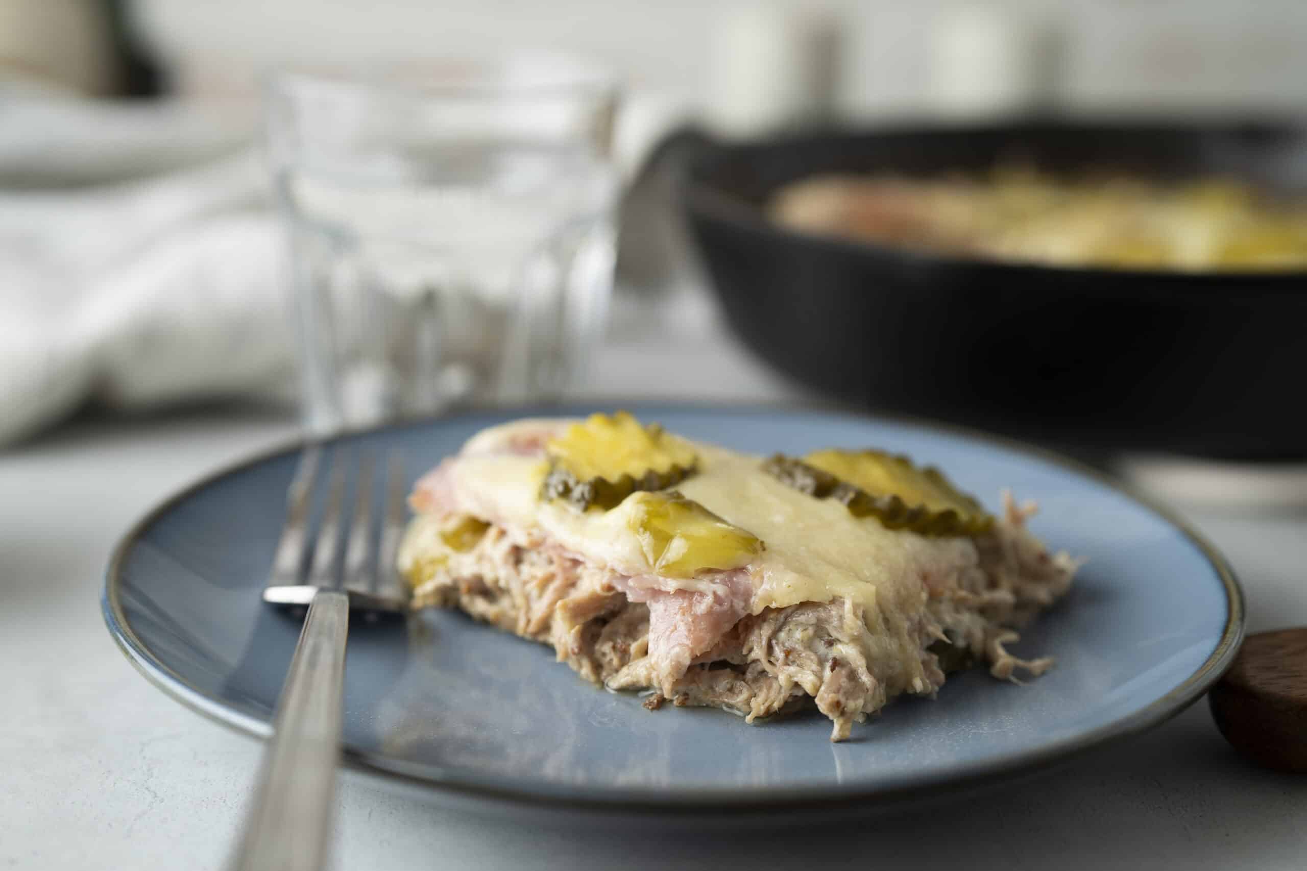 Baked chicken casserole with pickles and melted cheese served on a blue plate, with a fork, in a cozy home kitchen setting.