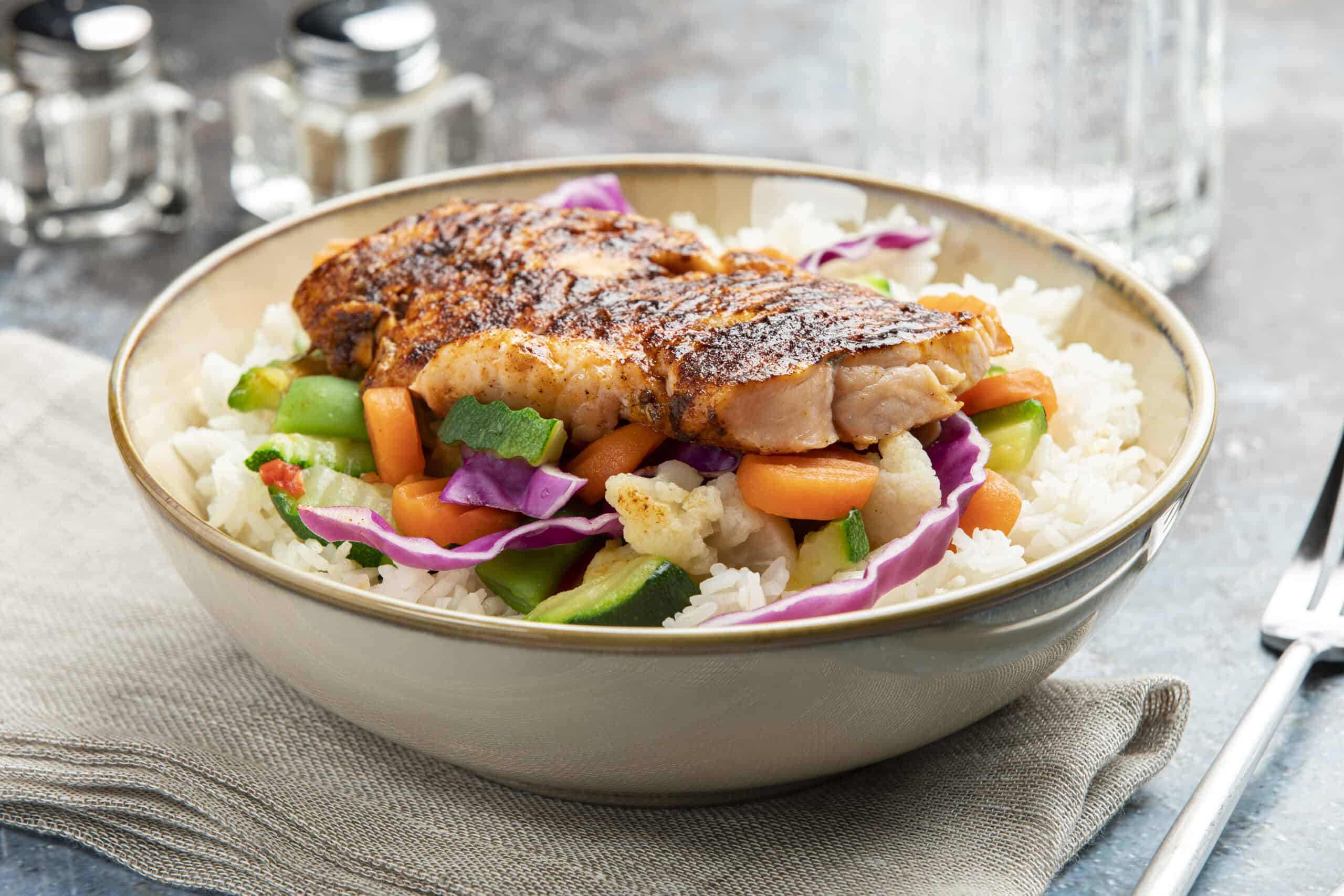 Juicy baked salmon fillet served over a bed of mixed vegetables and white rice in a beige bowl, garnished with colorful vegetables for a healthy and delicious meal.