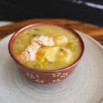 Creamy chicken and vegetable soup in a red floral-patterned bowl with potatoes, peas, and shredded chicken, served on a rustic wooden tray, perfect for comforting homemade recipes.