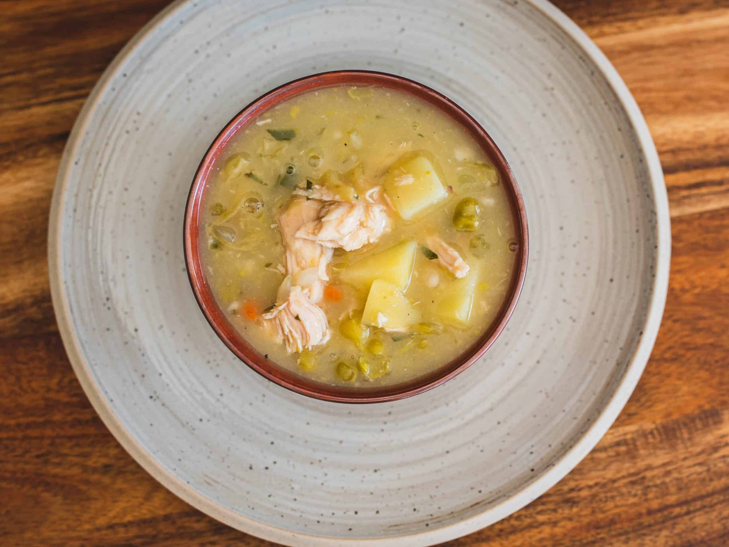 Tender chicken soup with potatoes, vegetables, and herbs served in a rustic bowl on a wooden table.