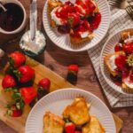 Fresh strawberries and strawberry-topped French toast with whipped cream and berry syrup on a rustic wooden table, perfect for a delicious breakfast or brunch.