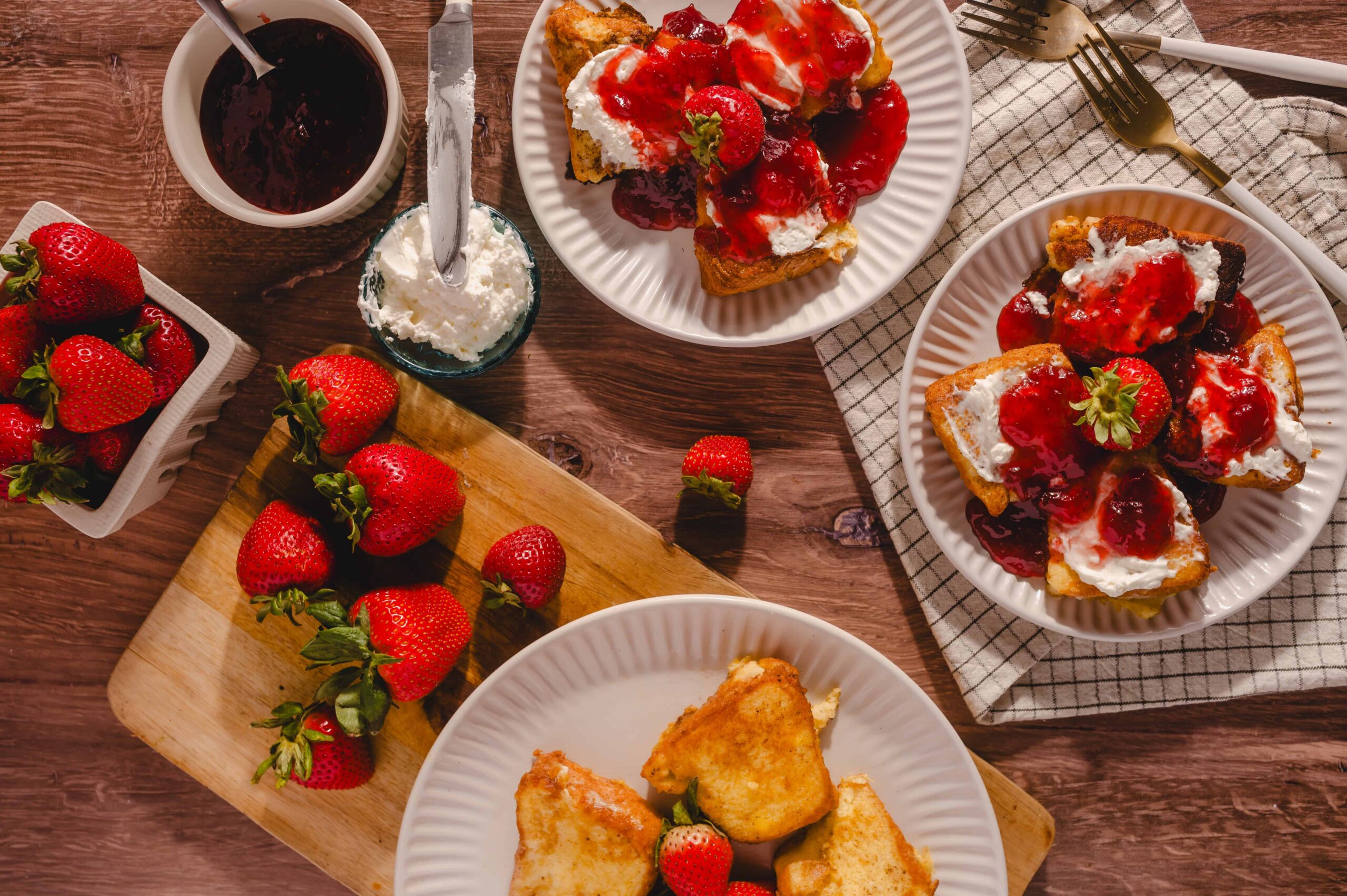 Fresh strawberries and strawberry-topped French toast with whipped cream and berry syrup on a rustic wooden table, perfect for a delicious breakfast or brunch.