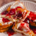 Sweet potato casserole with cranberry sauce and marshmallows on a paper plate, close-up of a fork taking a bite, highlighting the creamy texture and vibrant berry topping, perfect for holiday desserts.