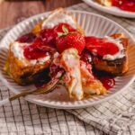 Fresh strawberry shortcake with whipped cream and strawberry topping served on a white plate. Cheesecake with strawberry sauce and fresh fruit garnished with a whole strawberry. Bright and delicious dessert ideal for summer or special occasions.