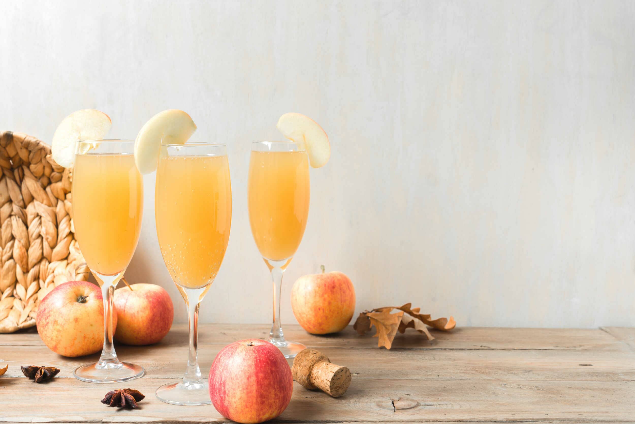Refreshing apple cider in elegant champagne flutes garnished with apple slices, set on a rustic wooden table with apples, dried leaves, and star anise for a cozy fall or holiday celebration scene.