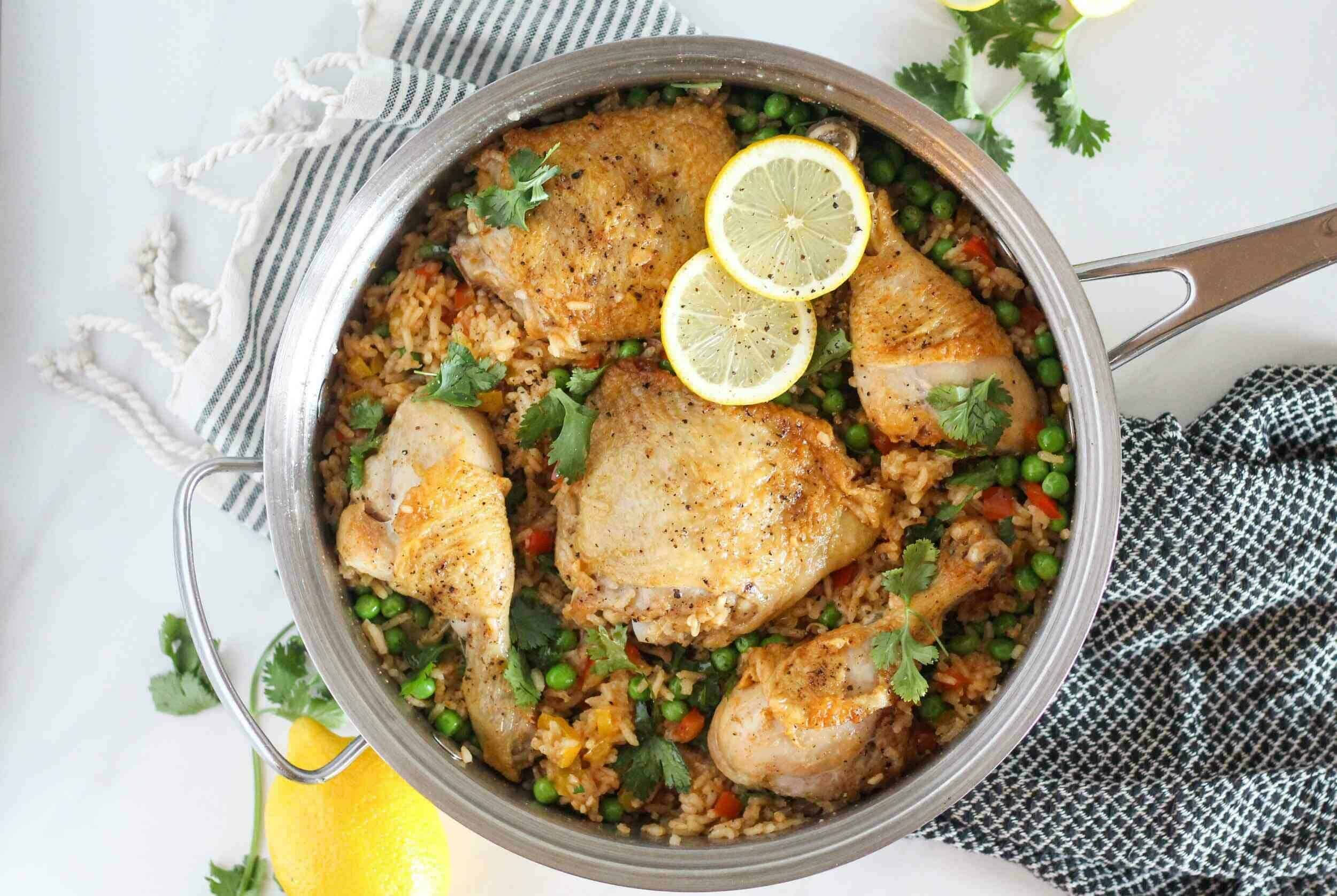 Succulent arroz con pollo baked in a skillet, garnished with fresh lemon slices and cilantro, perfect for a hearty, flavorful meal with tender chicken and colorful vegetables.