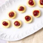 Mini cheesecakes with cherry topping on a white decorative platter, perfect for dessert recipes and celebrations.