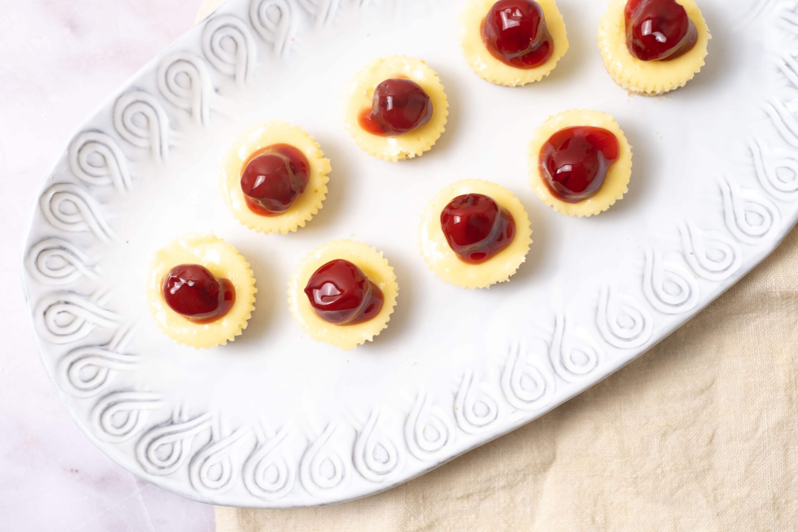 Mini cheesecakes with cherry topping on a white decorative platter, perfect for dessert recipes and celebrations.