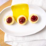 Sweet dessert with three mini cheesecakes topped with cherry sauce on a white oval plate.