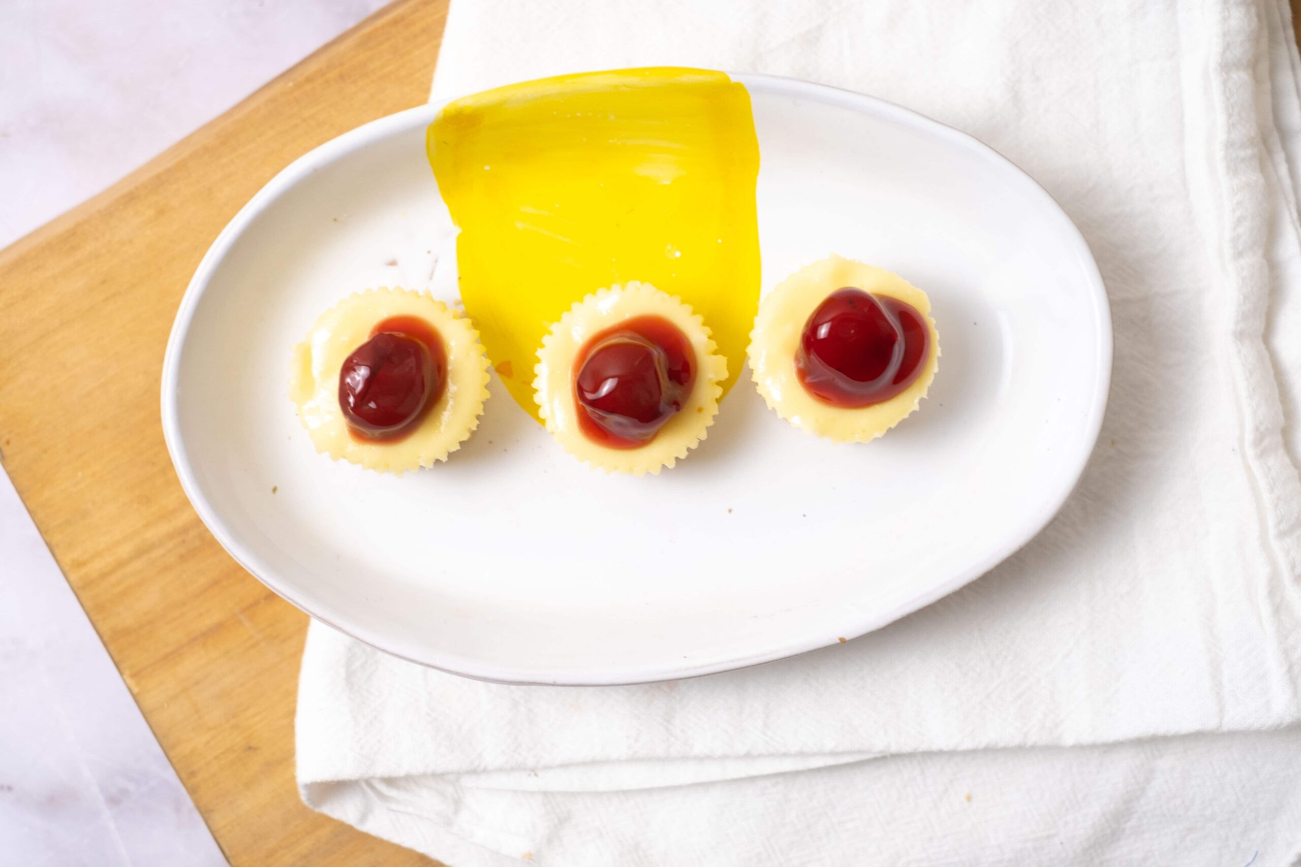 Sweet dessert with three mini cheesecakes topped with cherry sauce on a white oval plate.