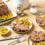 Juicy meatloaf with a savory mushroom gravy served with colorful mixed vegetables and pickles on a wooden table. Perfect comfort food recipe for family dinner.