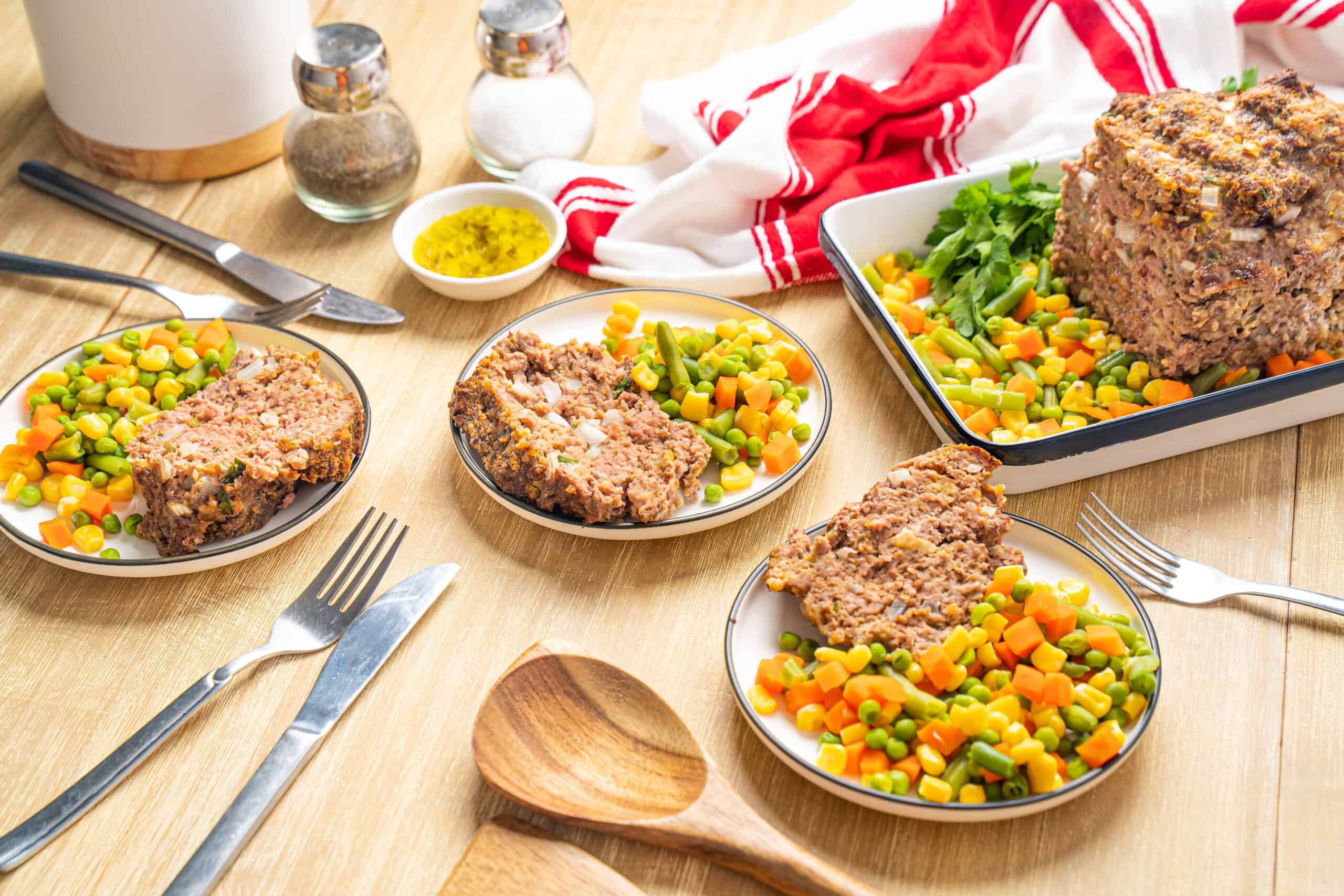 Savory meatloaf served with colorful mixed vegetables, including carrots, peas, and corn on a wooden table, highlighting hearty comfort food, home-cooked meal, and seasonal ingredients.
