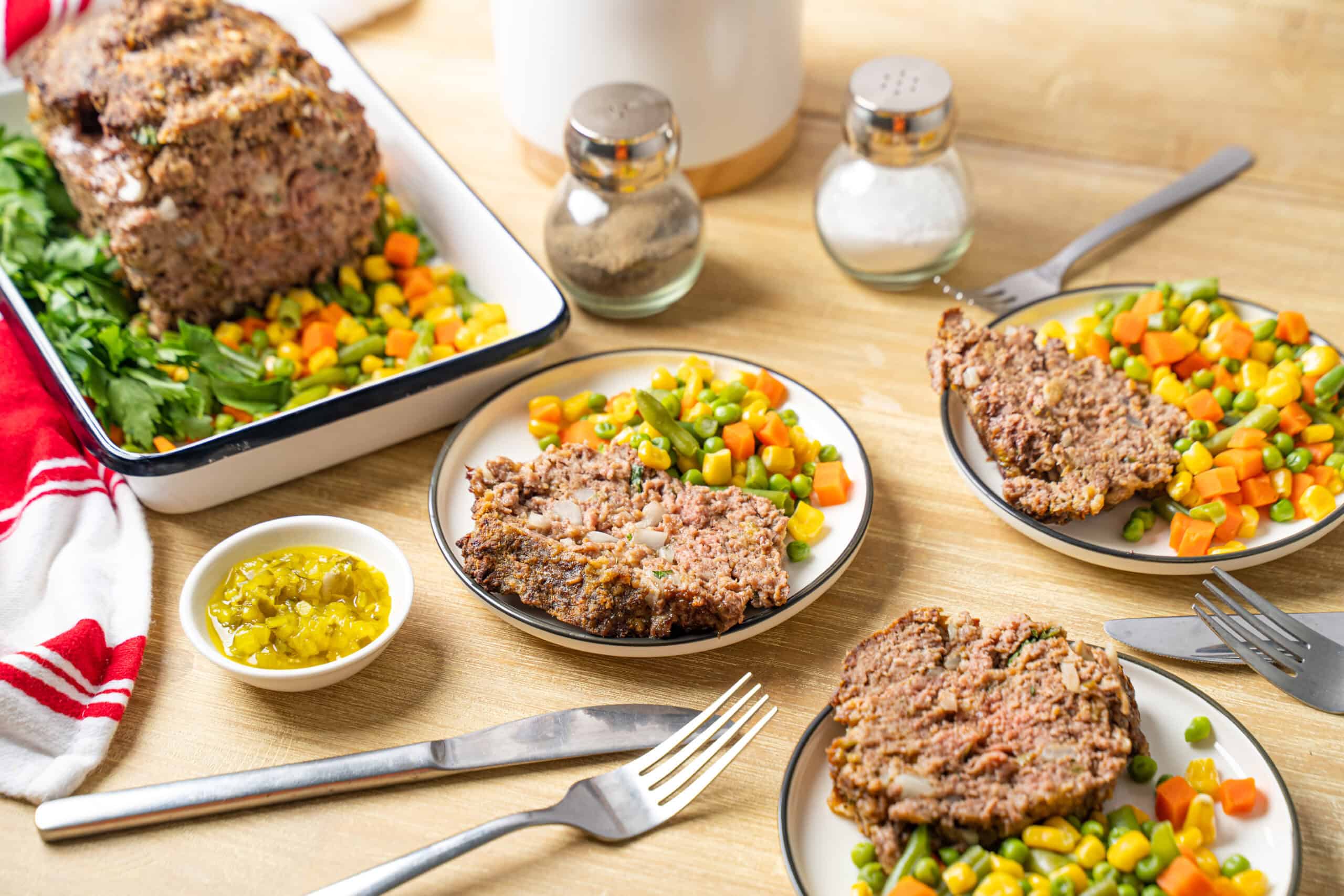 Juicy meatloaf with a savory mushroom gravy served with colorful mixed vegetables and pickles on a wooden table. Perfect comfort food recipe for family dinner.