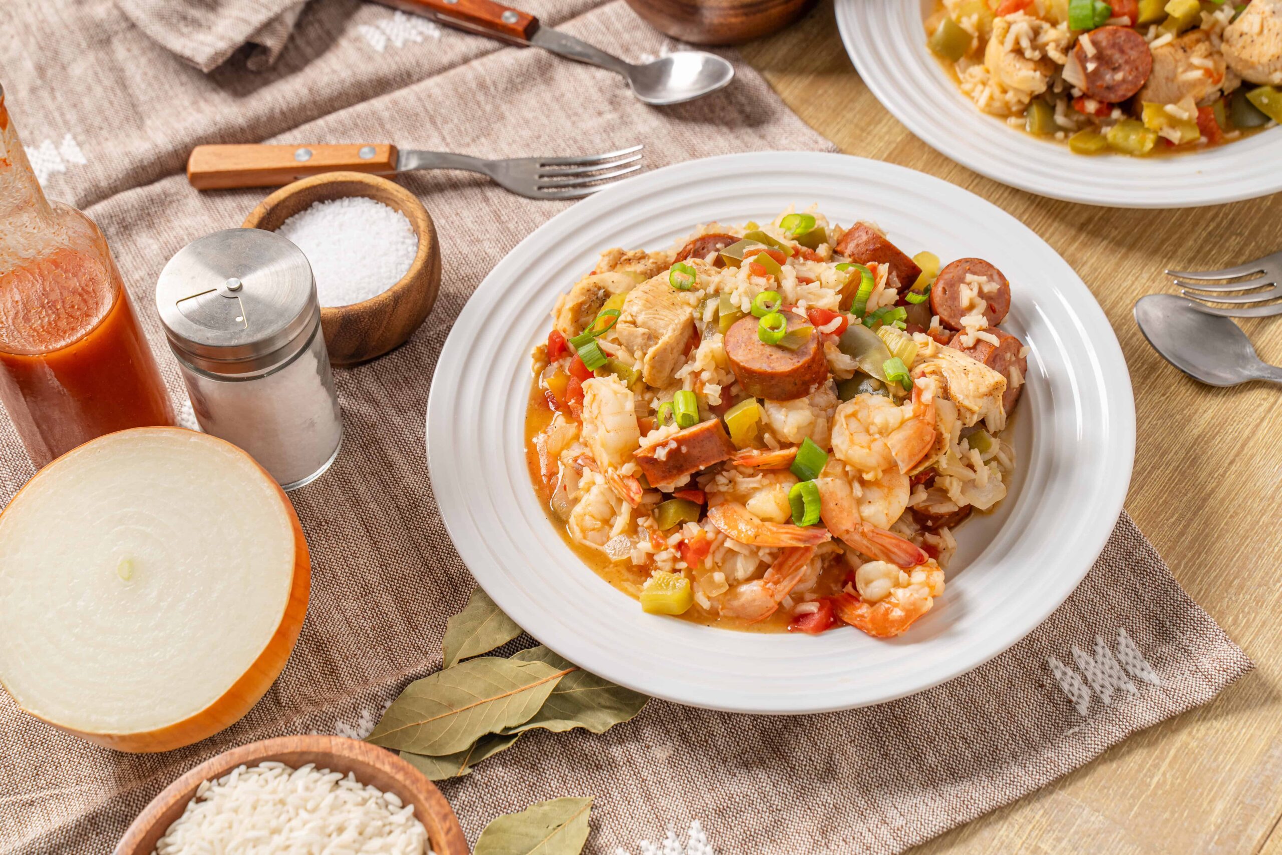 Savory seafood and sausage paella served on a white plate with garnishes, accompanied by ingredients like rice, onion, and spices, on a rustic wooden table.