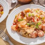 Savory shrimp and sausage jambalaya served with rice, vegetables, and green onions on a white plate. Perfect for a flavorful, hearty seafood and sausage dish.