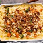 Creamy vegetable and chicken casserole topped with crispy fried onions in a white baking dish on rustic wooden table, garnished with fresh greens.