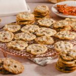Buttery chocolate chip cookies cooling on a wire rack with a plate of crispy bacon in the background.