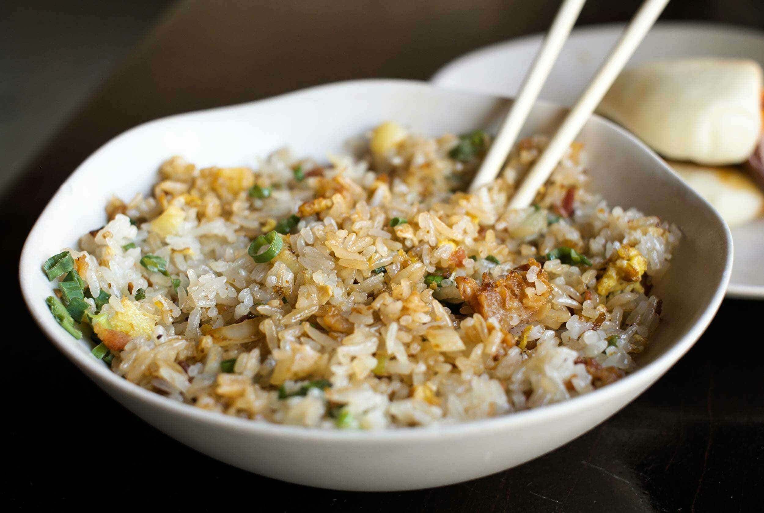 Stir-fried fried rice in a white bowl with chopped green onions and scrambled eggs, served with chopsticks and an Asian-style boiled egg on the side.