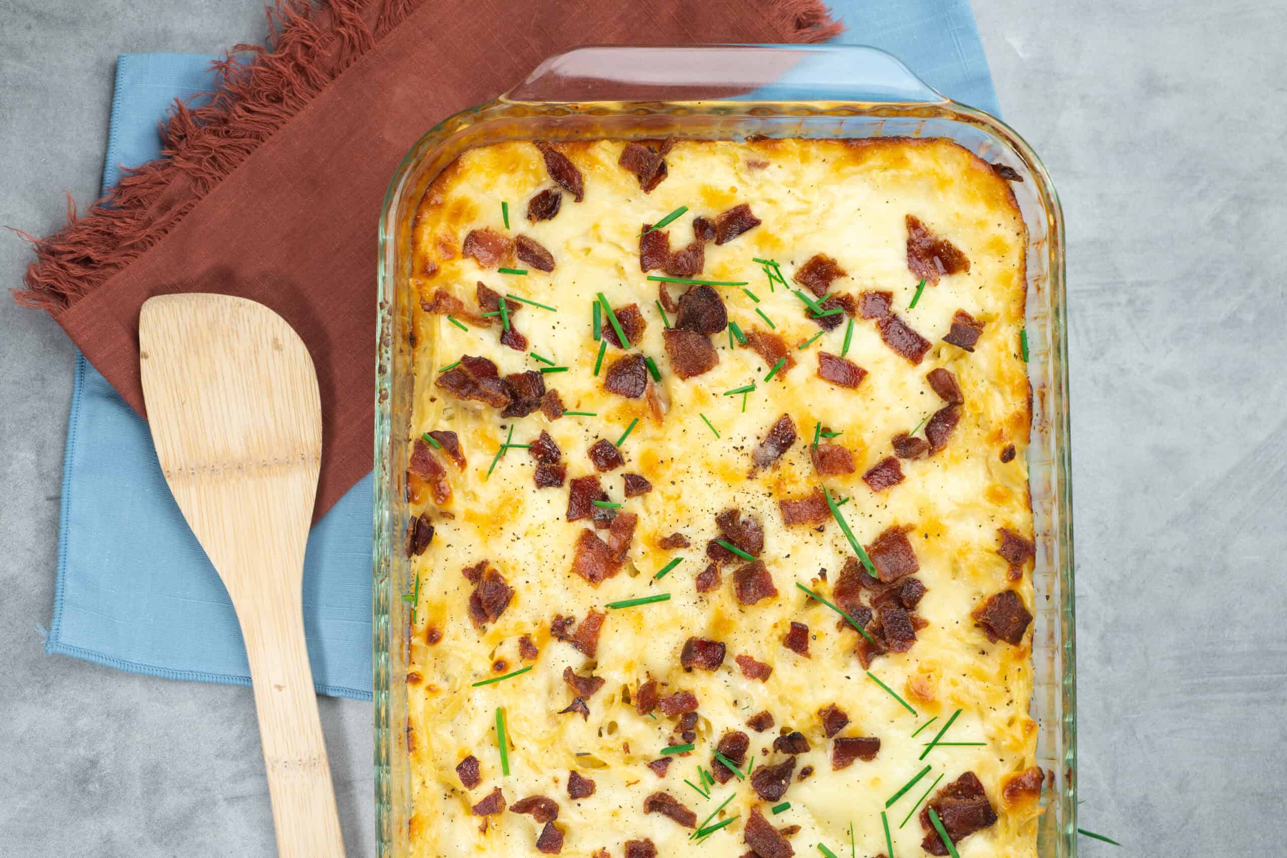 Baked cheesy potato casserole topped with crispy bacon bits and fresh chives served in a glass baking dish.