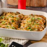 Baked stuffed peppers covered in melted cheese and garnished with fresh cilantro in a white baking dish.