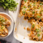 Cheesy baked chicken enchiladas with melted cheese and fresh cilantro on top, served in a white casserole dish and a separate plate for easy serving.