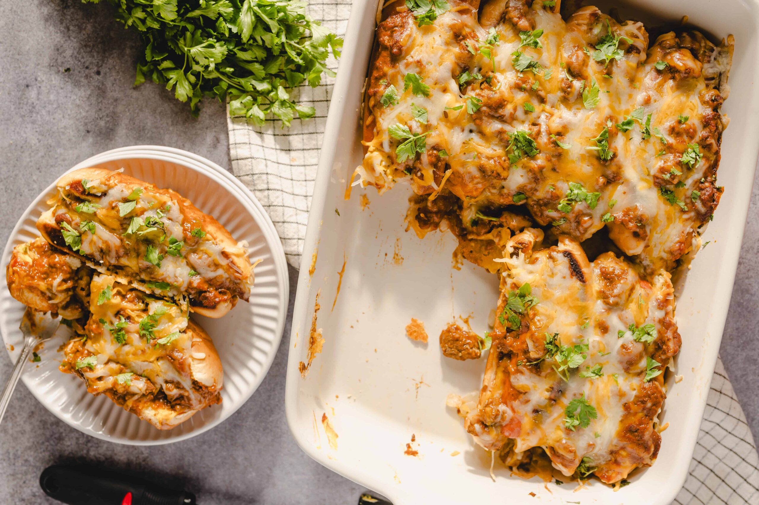 Cheesy baked chicken enchiladas with melted cheese and fresh cilantro on top, served in a white casserole dish and a separate plate for easy serving.