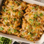Cheesy baked chicken casserole with melted cheese, ground meat, and fresh herbs in a white baking dish. Perfect comfort food easy to prepare for family dinners.